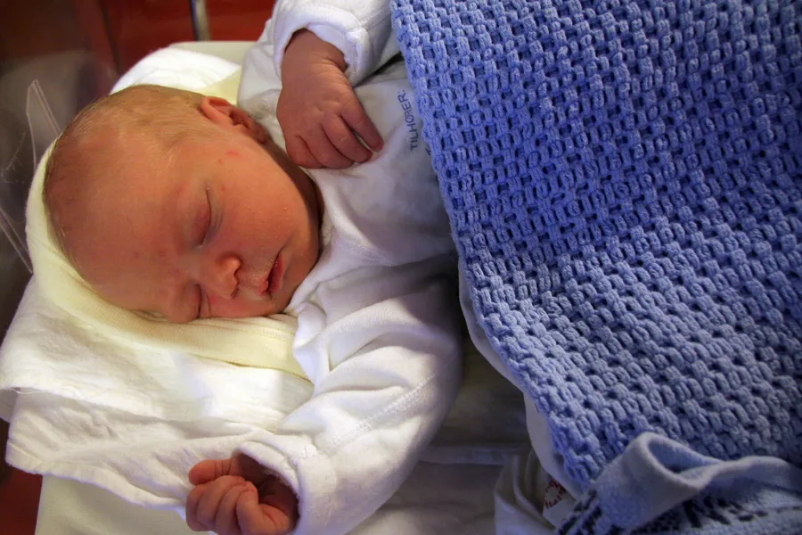 en nyfødt baby som ligger i et blått helseteppe