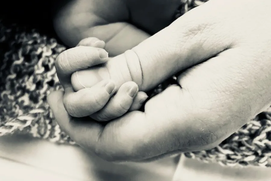 nyfødd babyhand som held i ei større hand