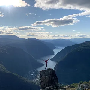 ei kvinne står på ein stein på eit fjell med flott utsikt over fjorden.