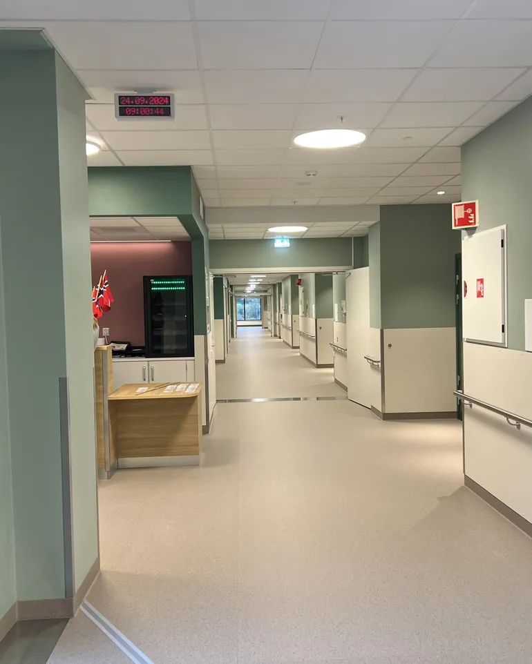 Ein lang sjukehusgang med grøne veggar