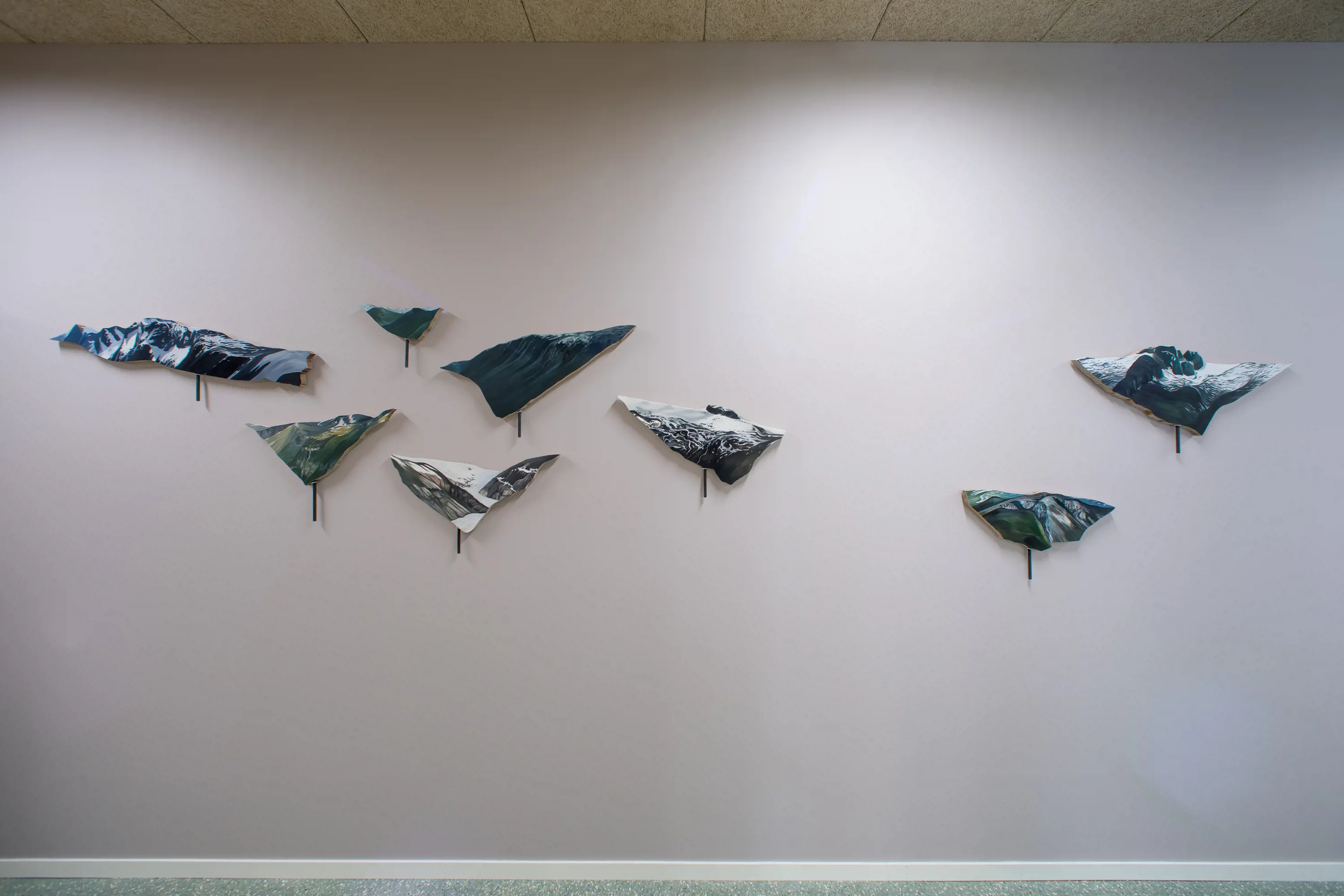 Ein kvit vegg med 8 kunstverk i ulike storleikar som heng på veggen og ser ut som fuglar. 