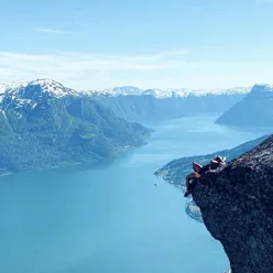 ein person ligg på ein fjellknaus og ser utover fjorden og fjella rundt
