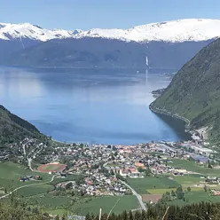 ei bygd med grøne fjellsider rundt ein fjord, og fjell med snø på toppane