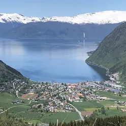 ei bygd med grøne fjellsider rundt ein fjord, og fjell med snø på toppane