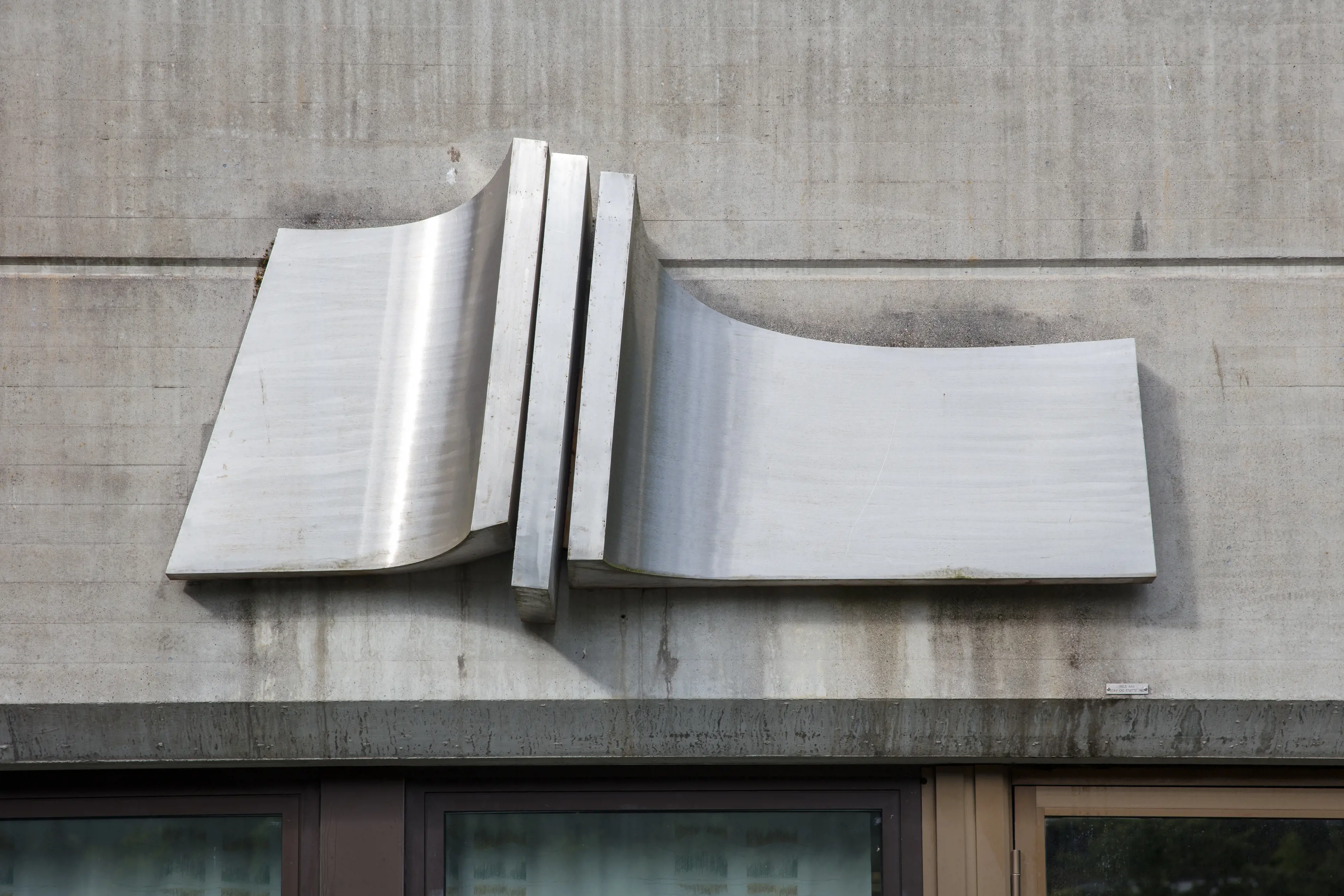 komposisjon i stål som er samansett av tre ståleiningar som heng på ein betongvegg utandørs