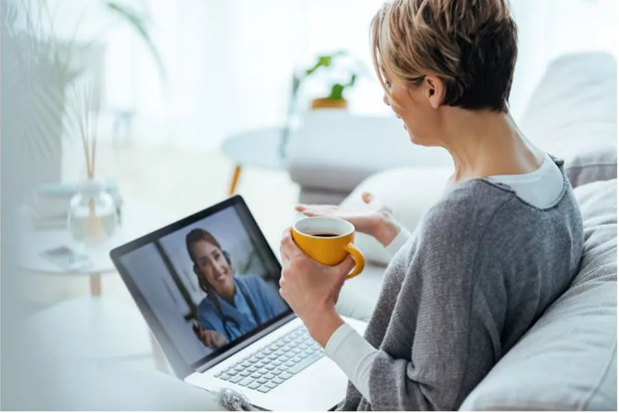 Ei kvinne som sit i sofaen og har videokonferanse med helsepersonell